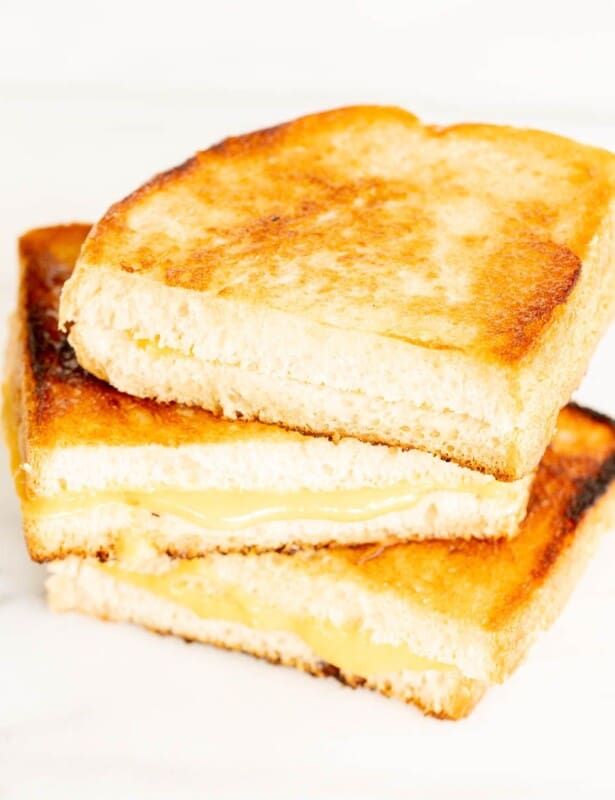 A stack of sliced grilled cheese with mayonnaise on a white marble surface.