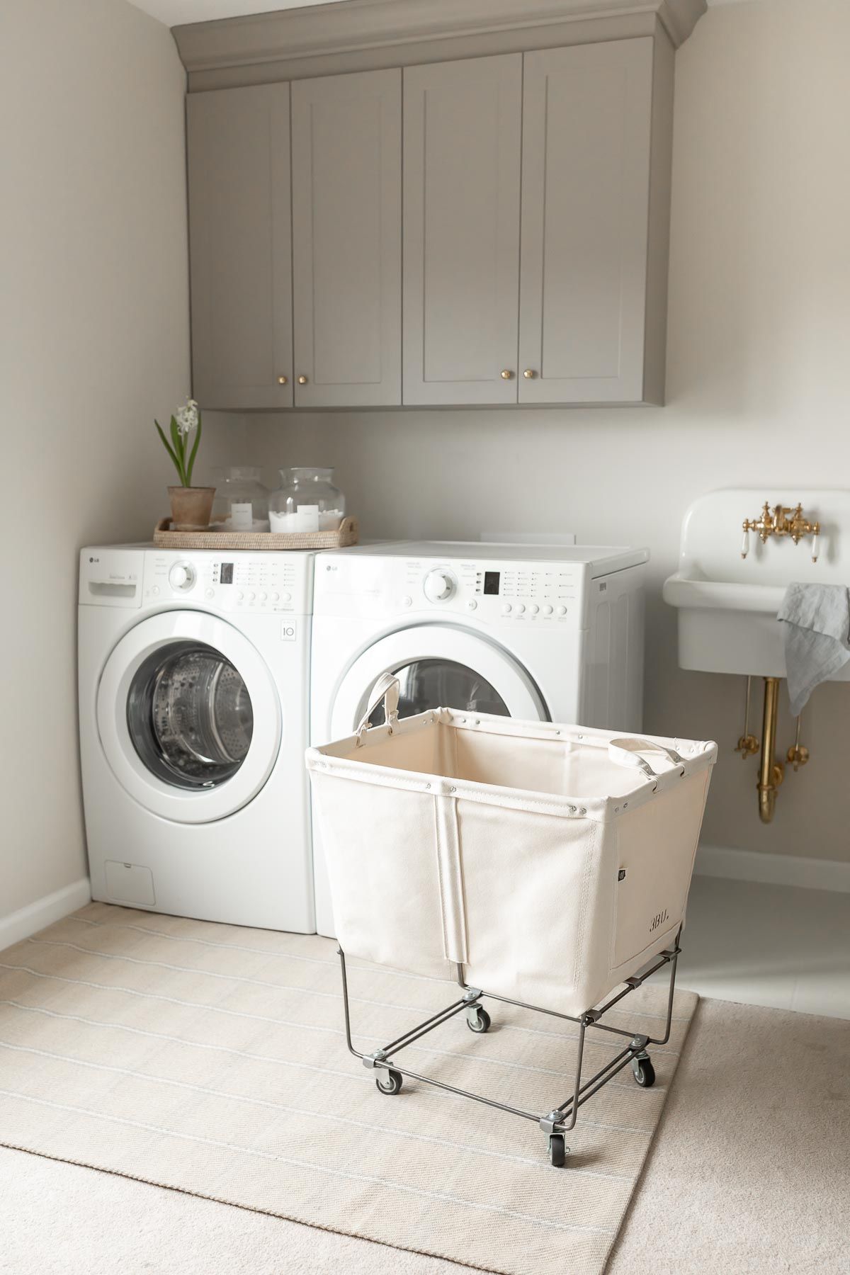 A laundry room with gray cabinets, a white washer and dryer, and a beige rug on carpet flooring.