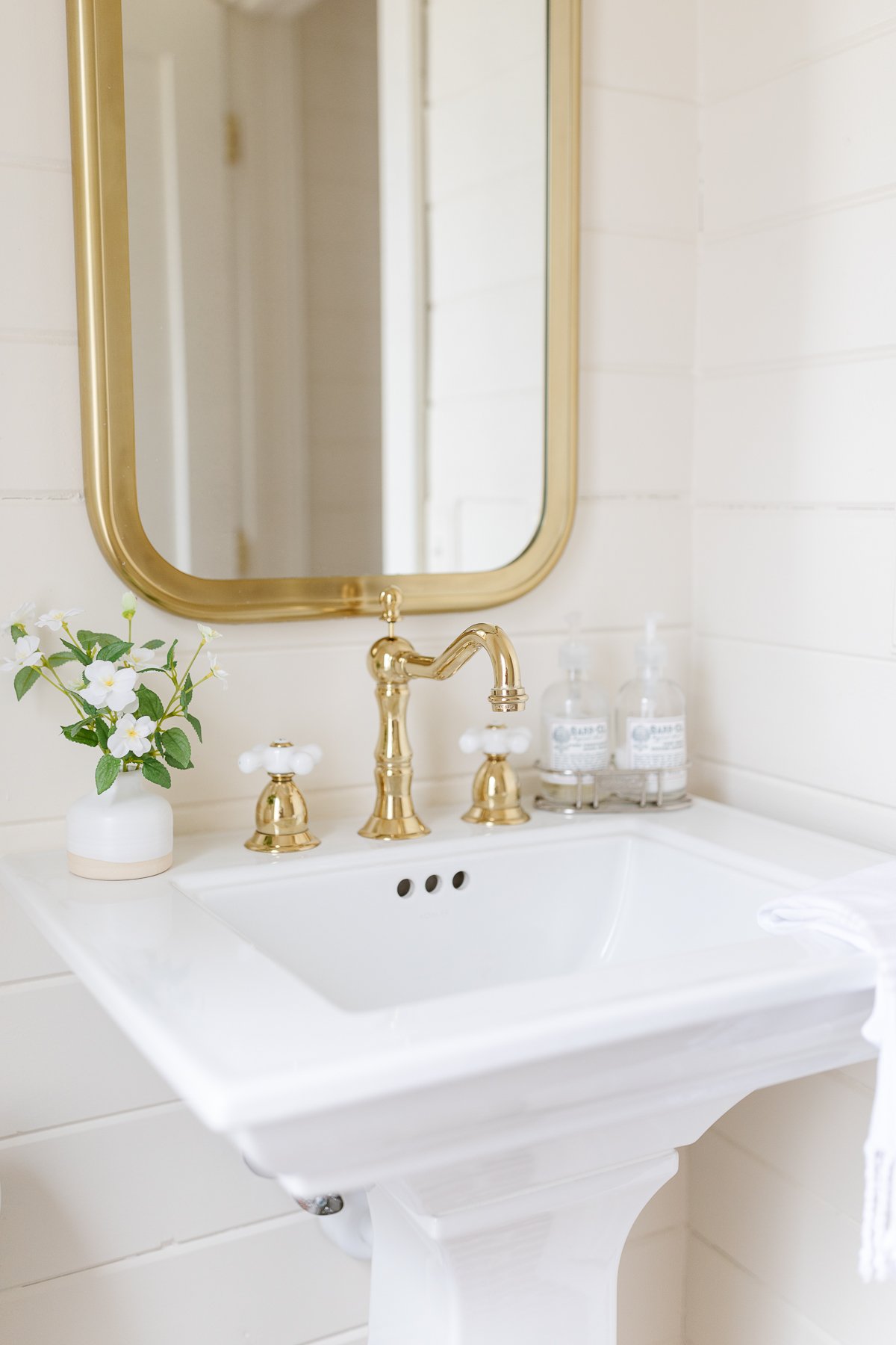 A white bathroom with a gold sink and mirror that makes the small room look bigger.