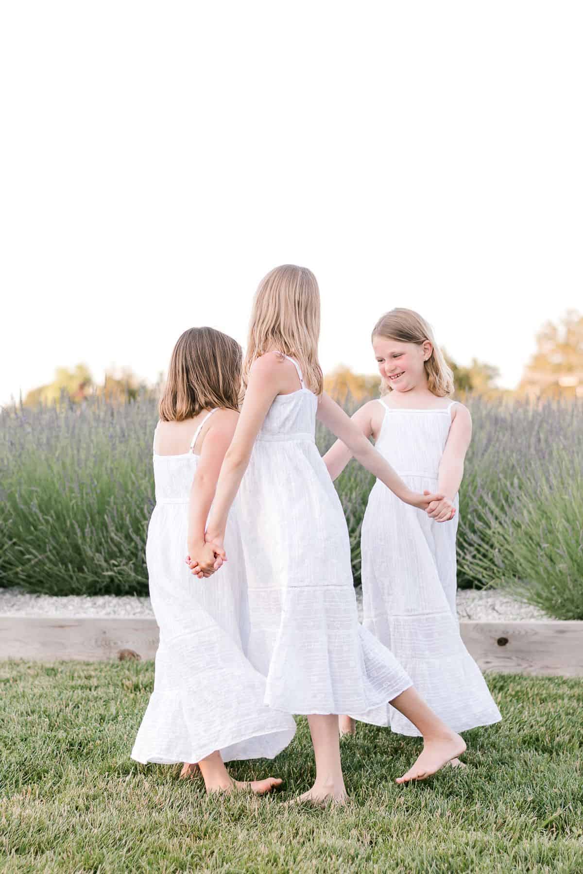 Three little girls in white dresses dancing in a field of english lavender.