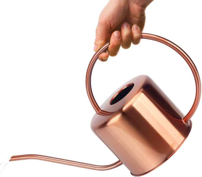 A hand holding a copper colored watering pitcher against a white background.