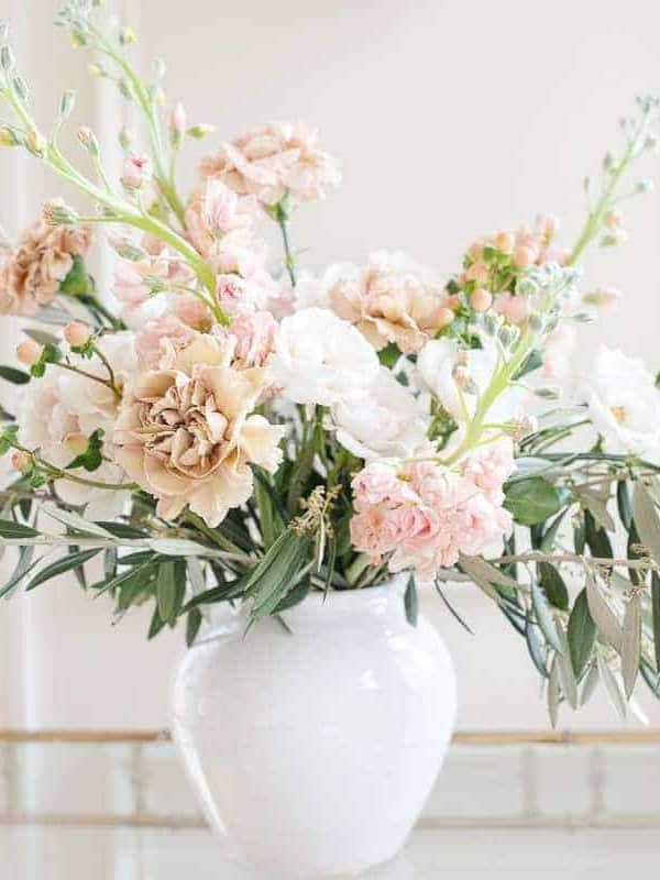 Antique carnations, stock and greenery in a white vase against a white background.