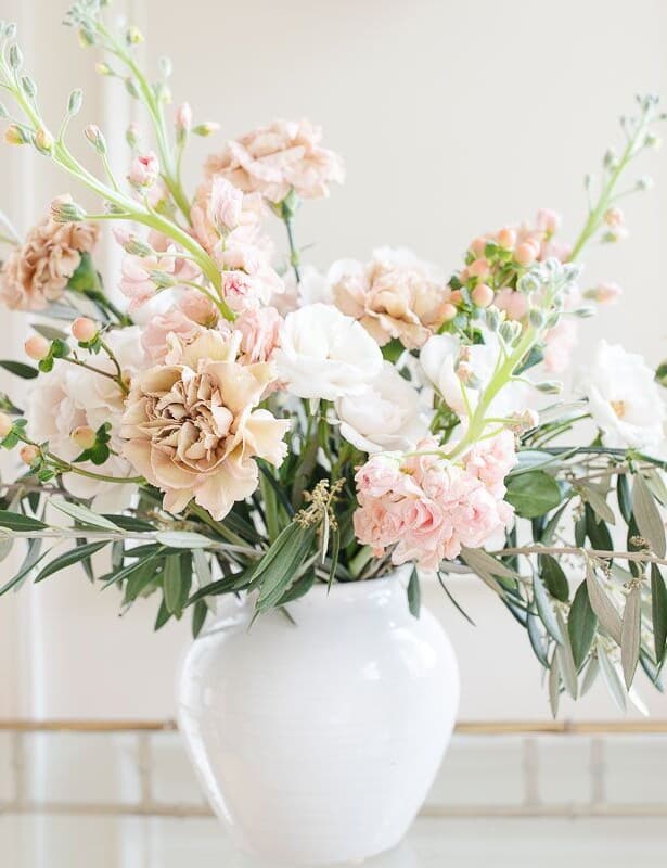 Antique carnations, stock and greenery in a white vase against a white background.