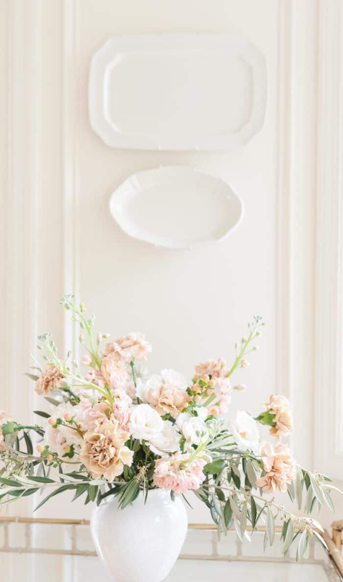 Antique carnations, stock and greenery in a white vase against a white background.