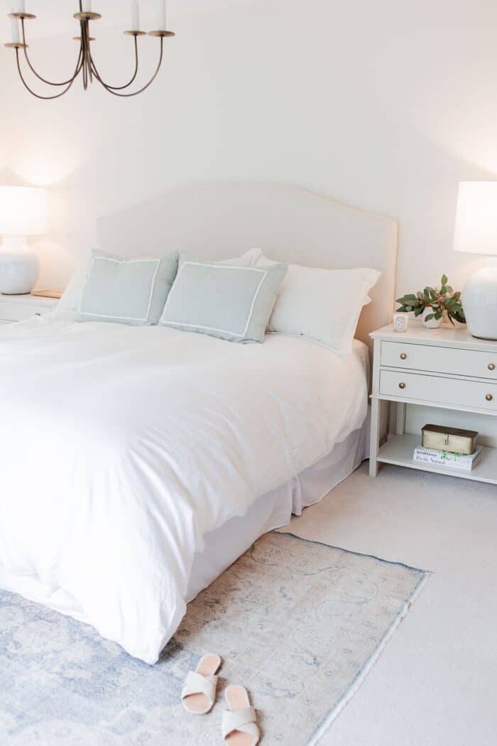 A white bedroom with a bedroom rug placement of a vintage rug under the bed.