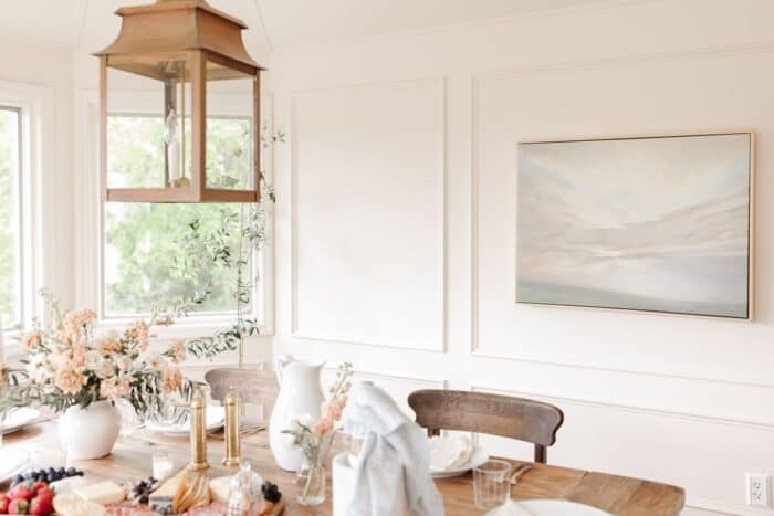 A white vase with a carnation arrangement on a wooden farm table in a cream dining room.