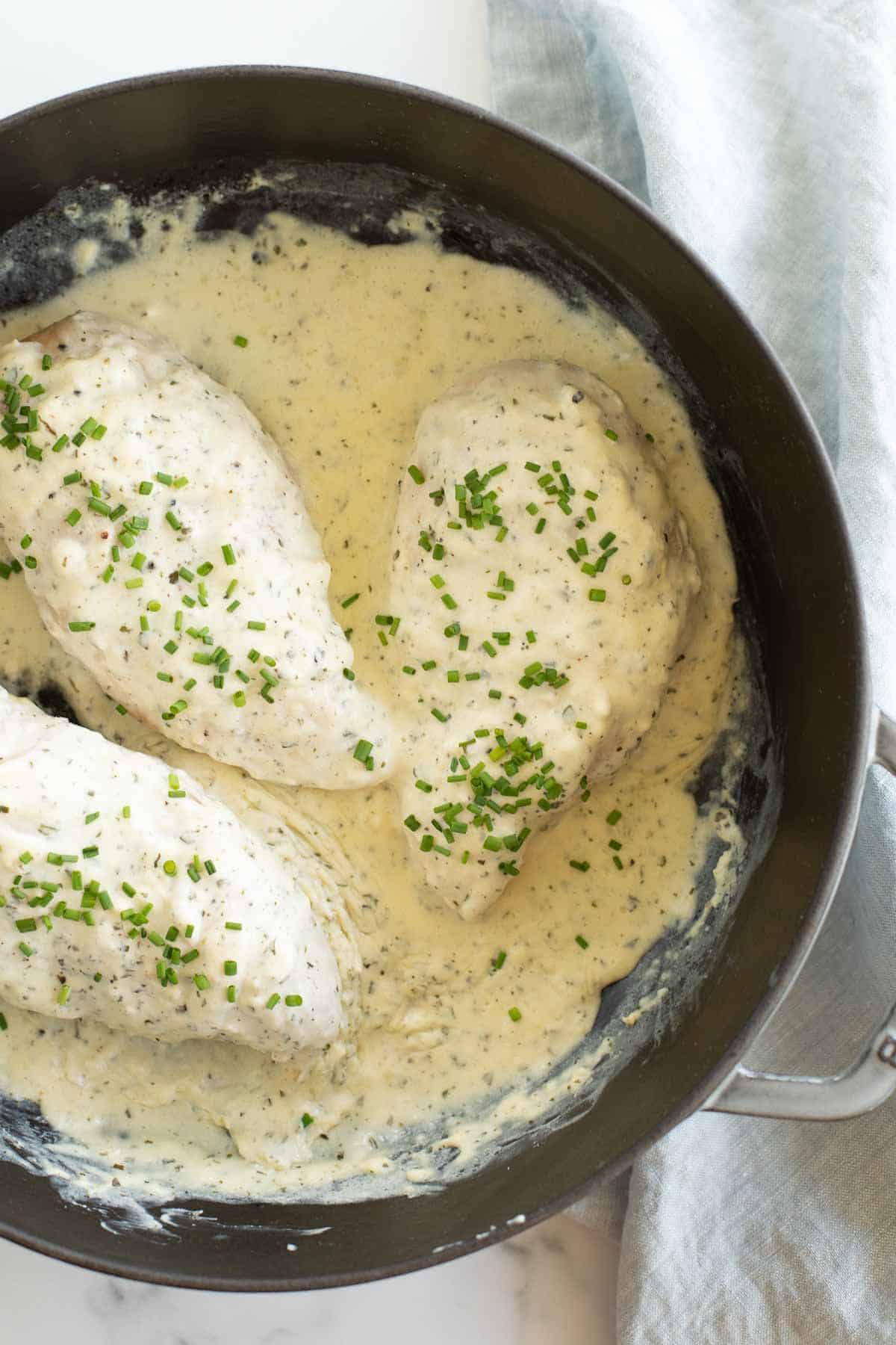 Three Boursin chicken breasts in a cast iron skillet, surrounded by creamy sauce.