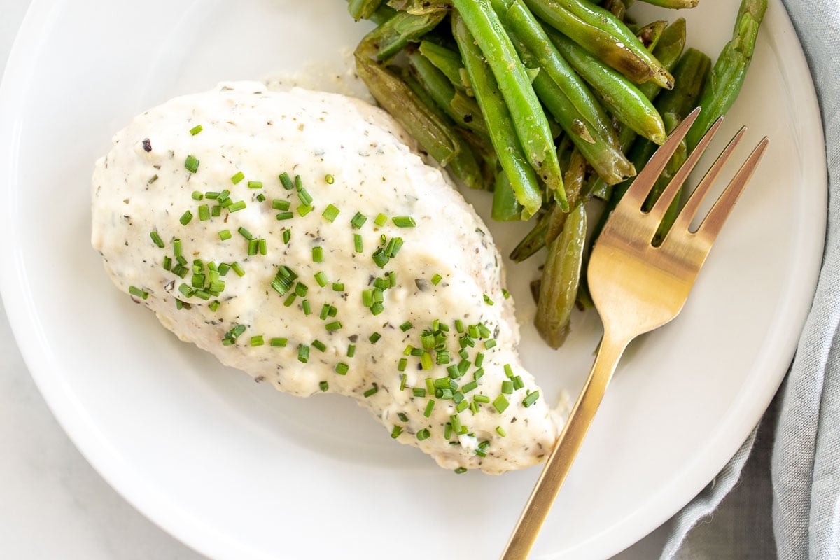 A white plate with a baked boursin chicken breast and green beans.