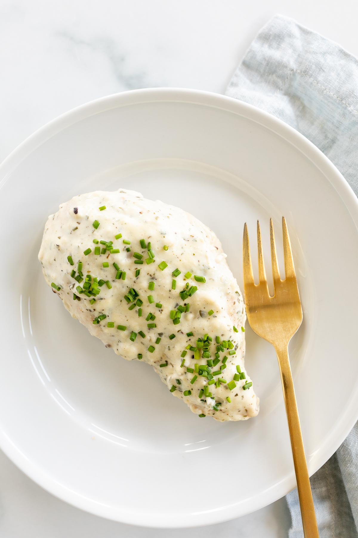 A white plate with a baked boursin chicken breast and a gold fork.