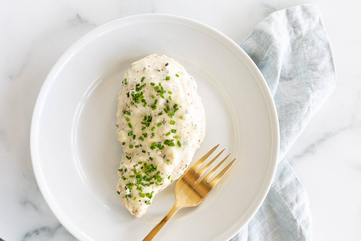 A white plate with a baked boursin chicken breast and a gold fork.