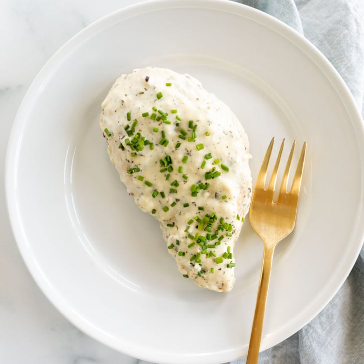 A white plate with a baked boursin chicken breast and a gold fork.