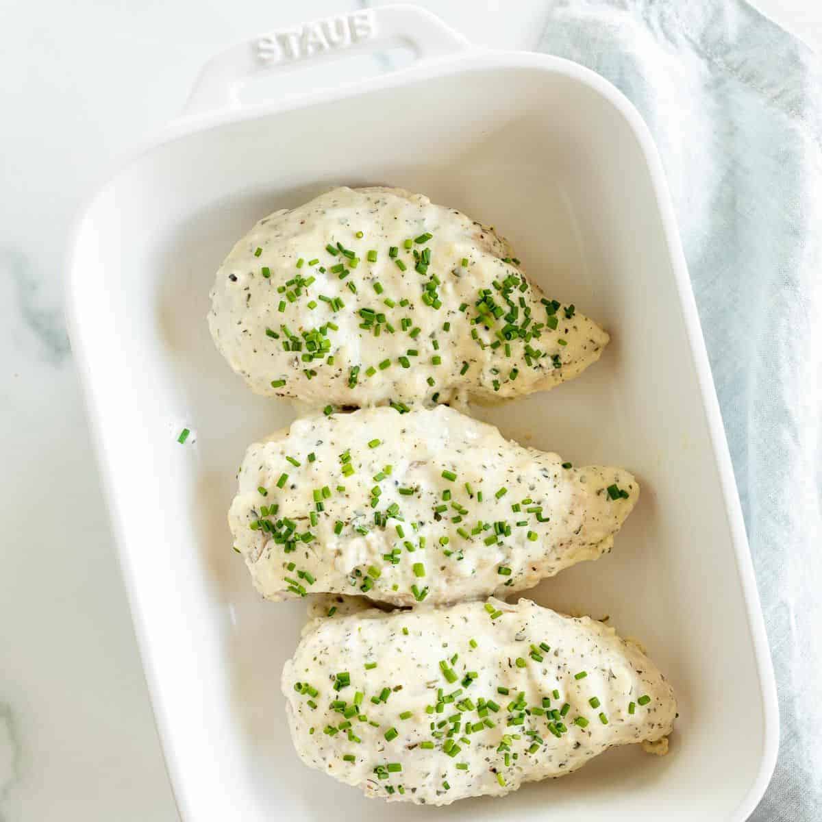 A white baking dish with baked Boursin chicken breast topped with chopped chives.