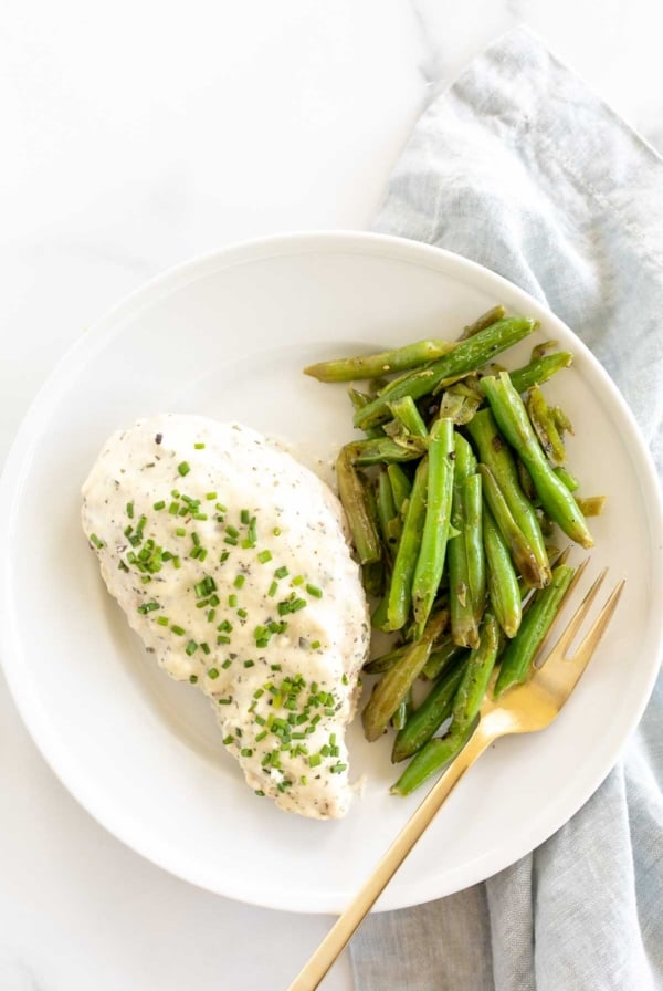 A white plate with a baked boursin chicken breast and green beans.