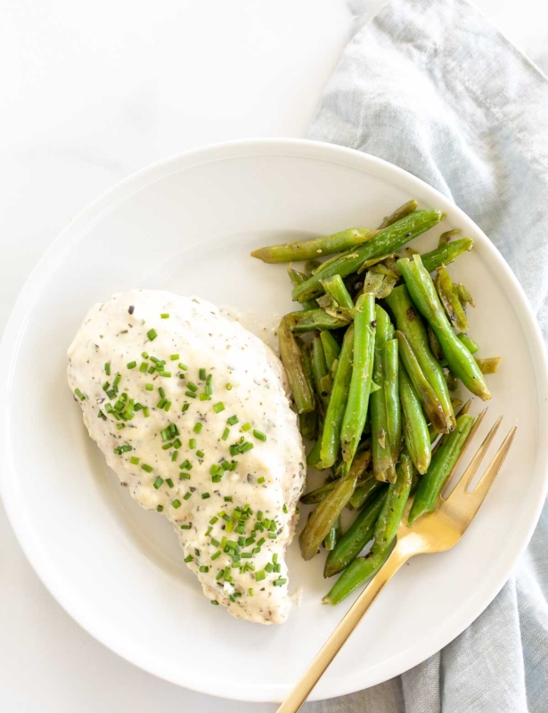 A white plate with a baked boursin chicken breast and green beans.