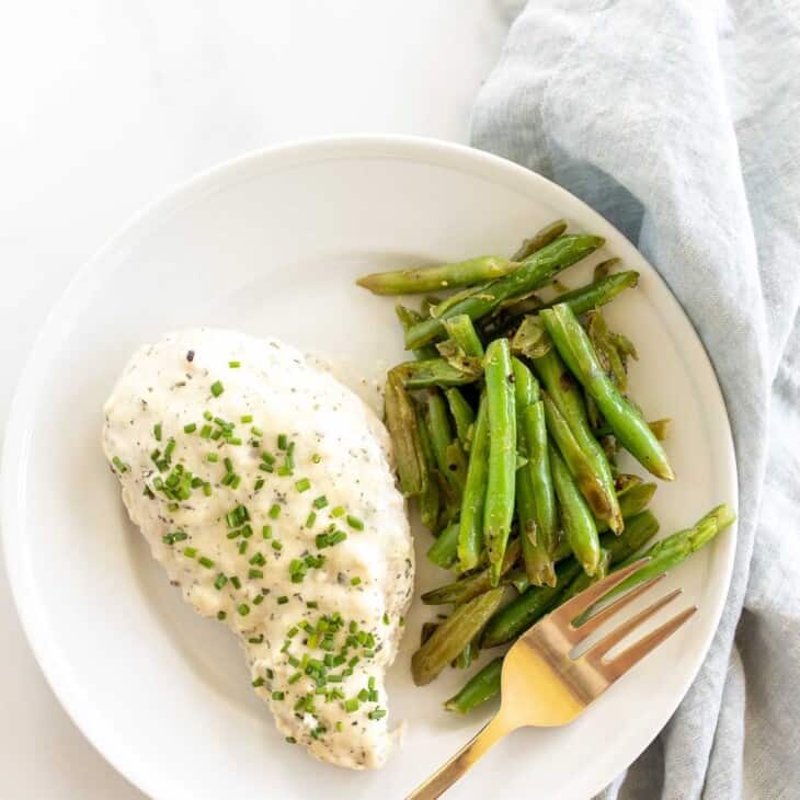 A Boursin chicken breast served with green beans on a white plate with a gold fork.