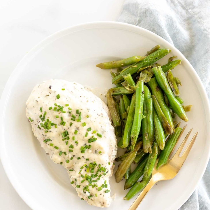 A white plate with a baked boursin chicken breast and green beans.
