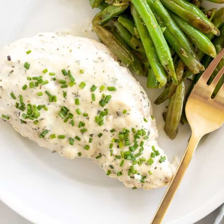 A Boursin chicken breast served with green beans on a white plate with a gold fork.