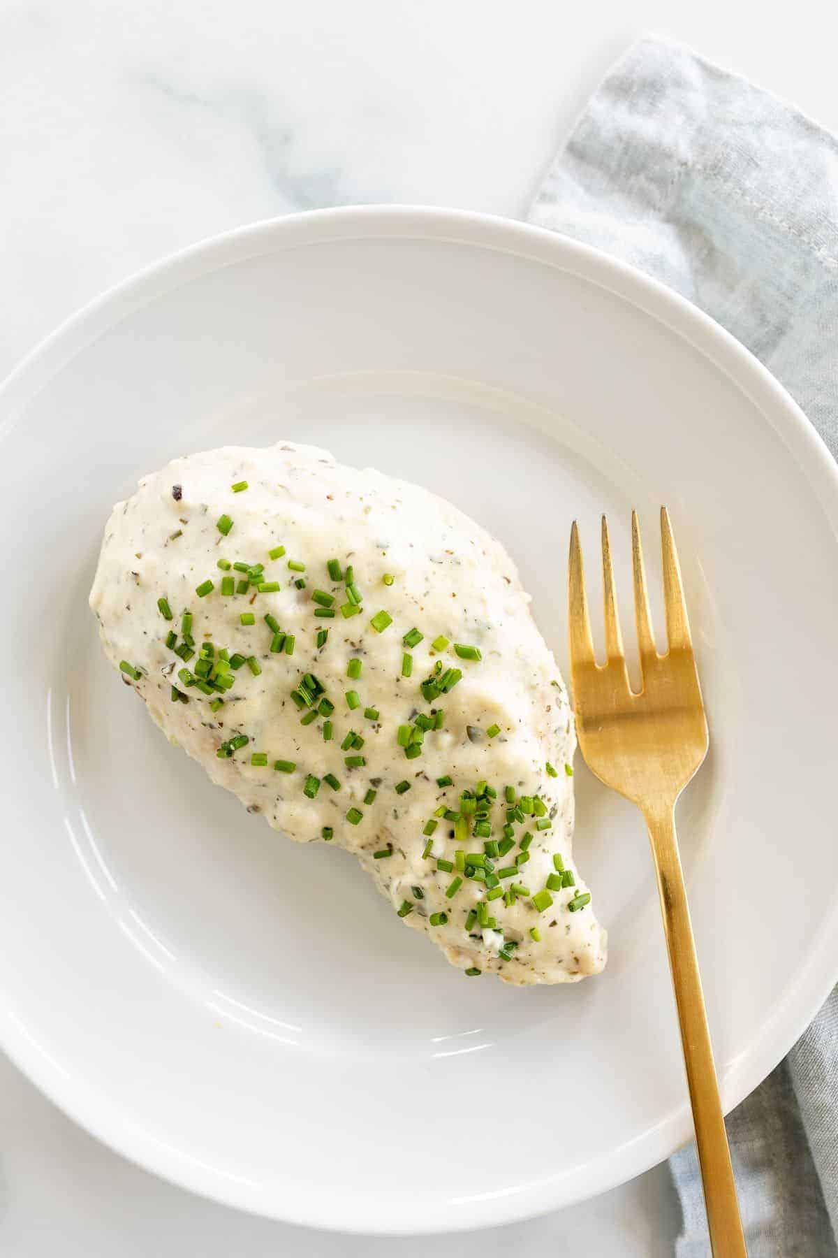 A Boursin chicken breast served on a white plate with a gold fork.