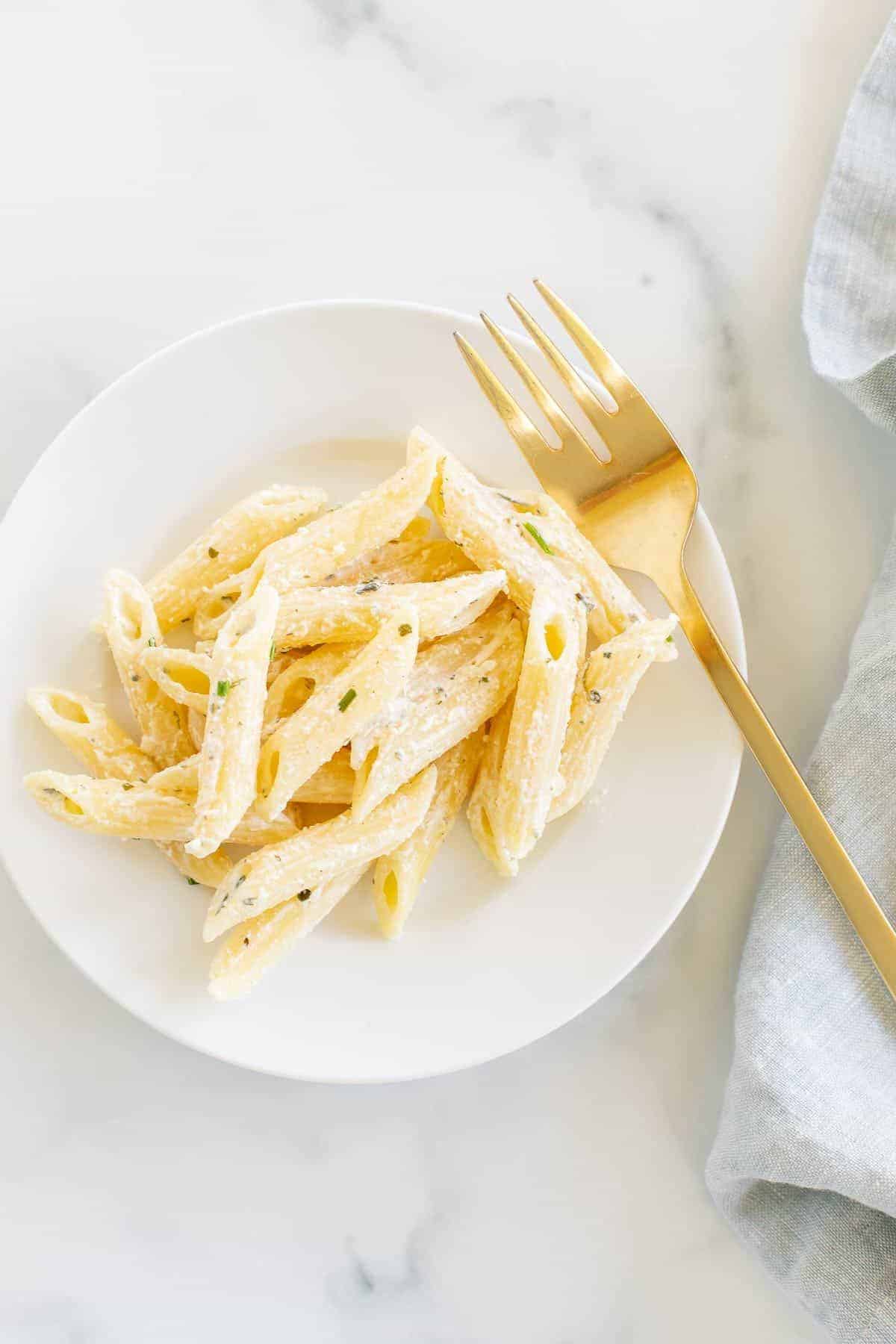 A white plate with Boursin pasta, gold fork lifting up a bite.