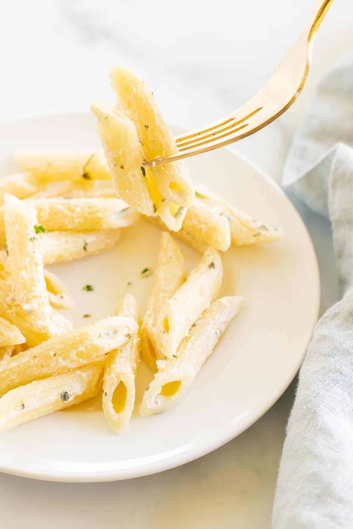 A white plate with Boursin cheese pasta, gold fork lifting up a bite.