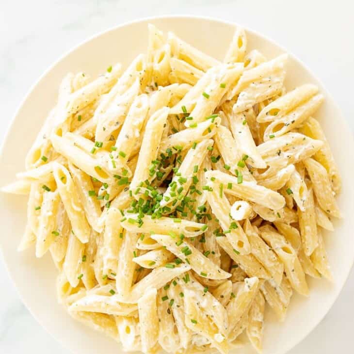 A white serving bowl full of Boursin pasta topped with chives.