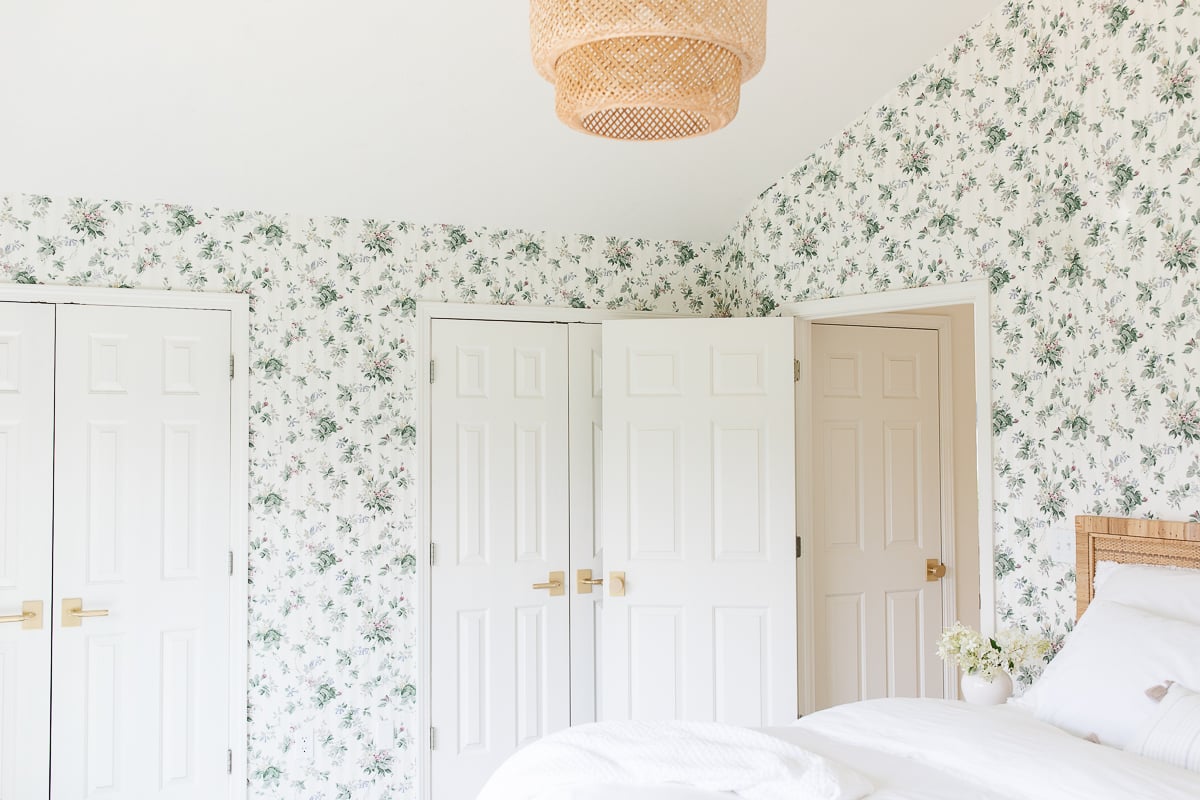 A bedroom with floral wallpaper with modern brass door knobs on the doors.