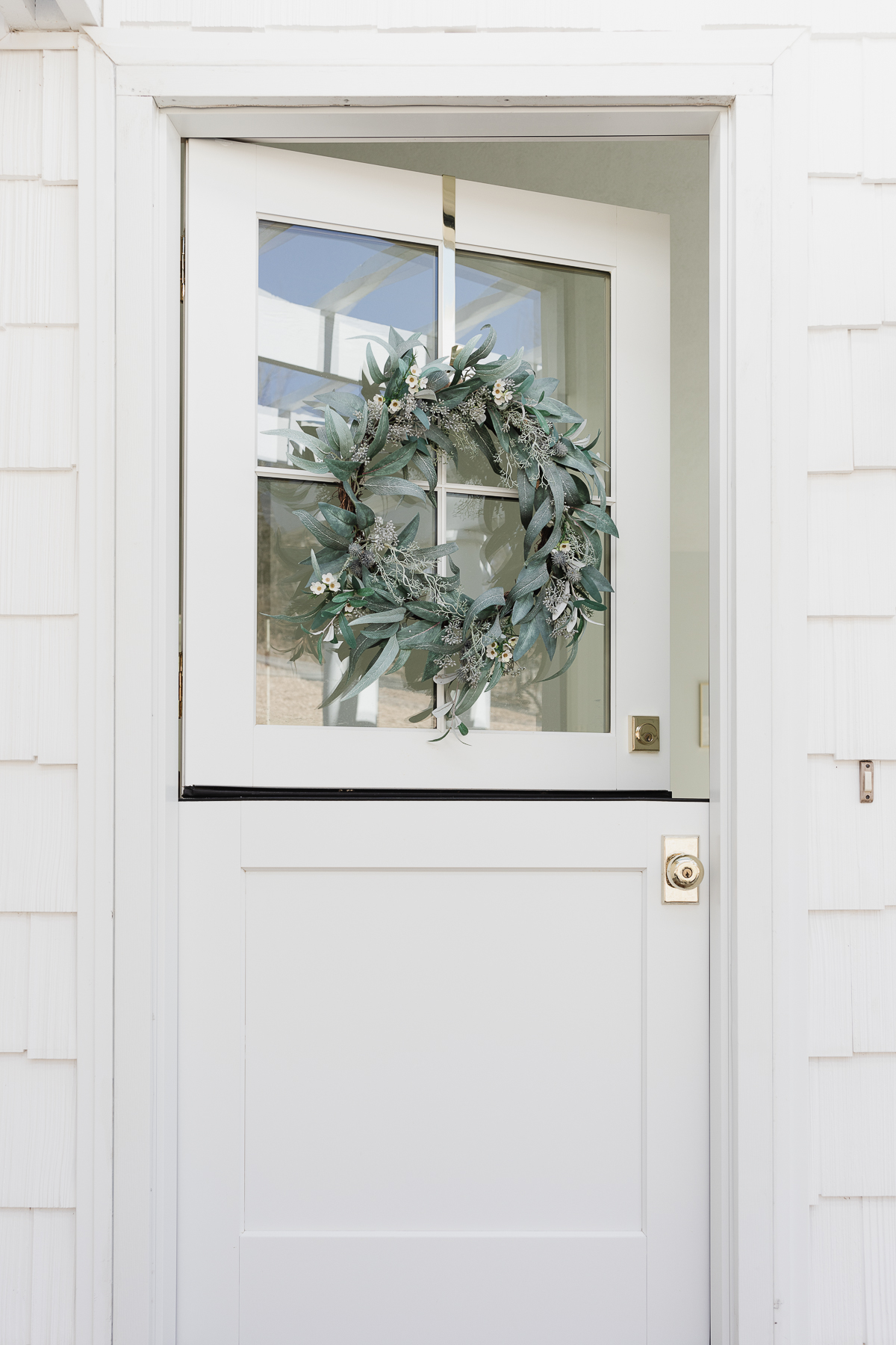 A white Dutch door on a white house, featuring a brass door knob.