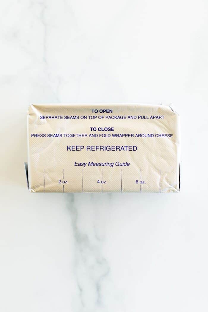 A block of cream cheese wrapped in foil packaging on a marble surface.
