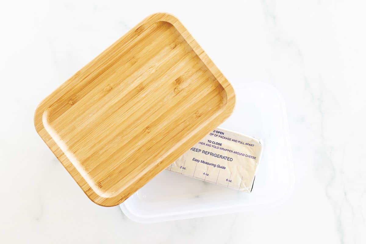 A block of frozen cream cheese inside a container with a bamboo lid.