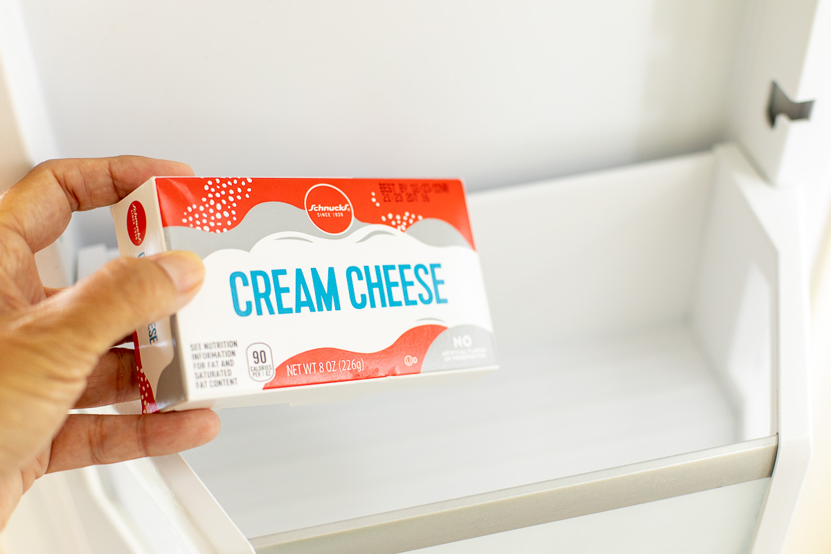 Person placing a package of cream cheese in an open freezer drawer to freeze.