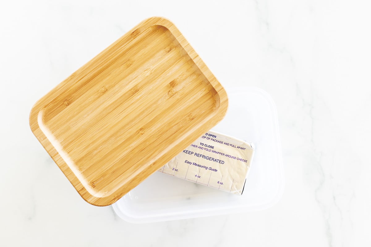 A bamboo tray alongside a wrapped stick of butter with a "can you freeze" label on a marble surface.