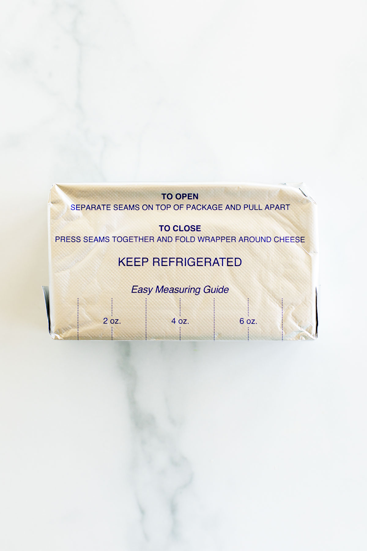 A block of cream cheese in a gold foil wrapper with opening instructions and a measuring guide, along with tips on how to freeze, printed on it.