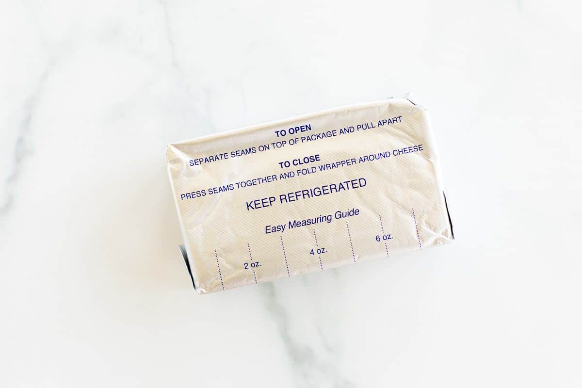 A block of cream cheese wrapped in foil packaging on a marble surface.