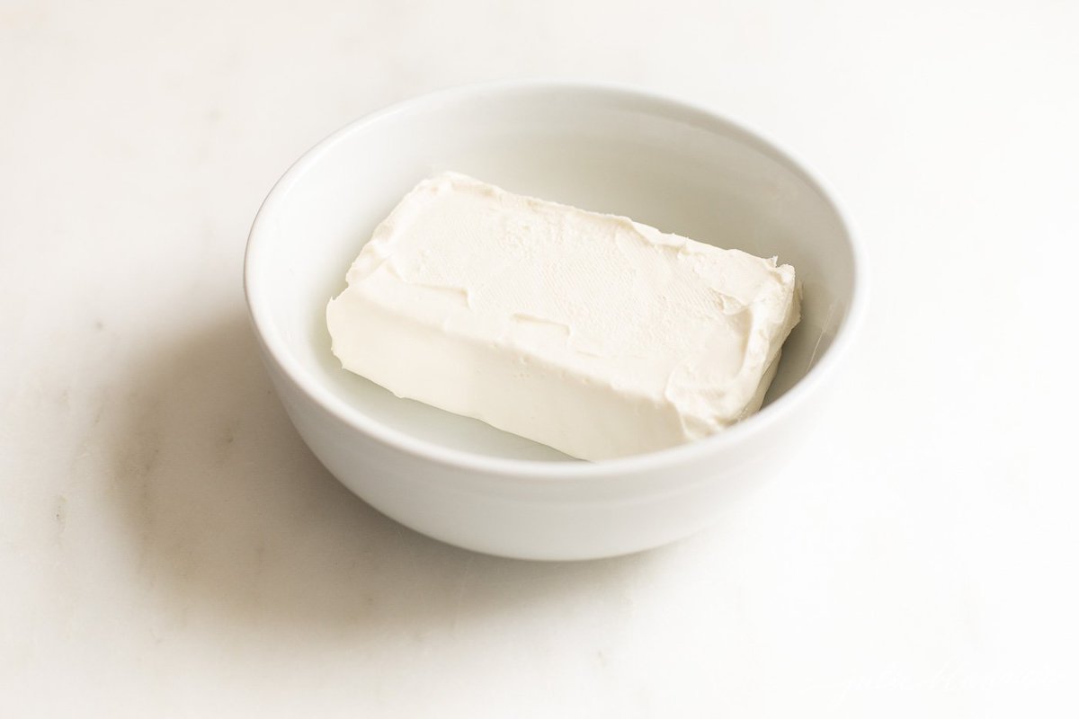 A block of cream cheese, which you can freeze, in a white bowl on a light surface.