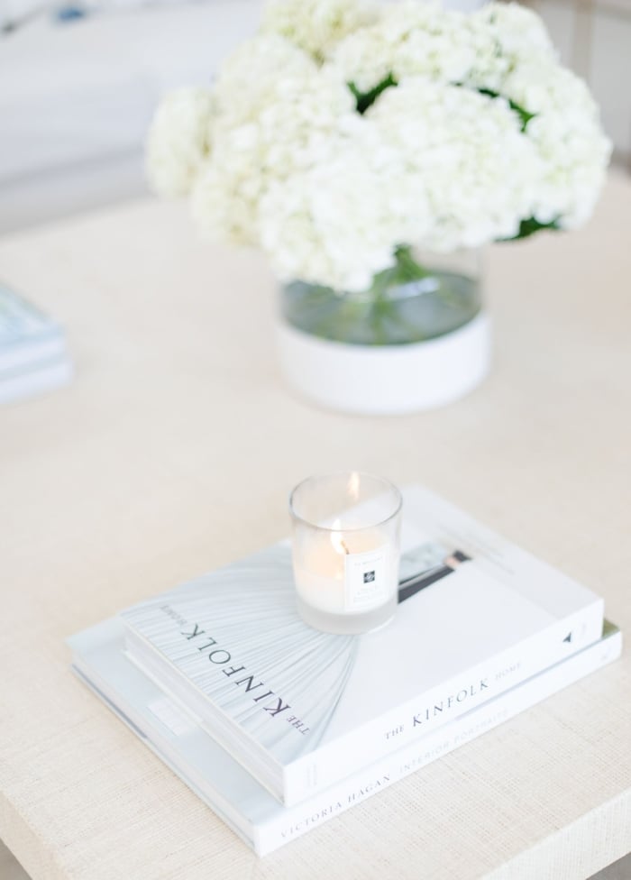 A stack of decorative books on a coffee table, with a lit candle on top