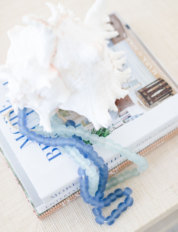 A raffia coffee table topped with a sea shell on top of blue and white decorative books