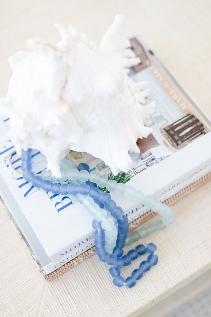 A raffia coffee table topped with a shell on top of blue and white decorative books
