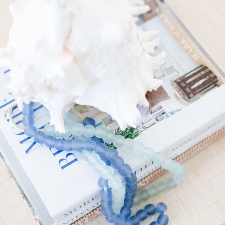 A raffia coffee table topped with a sea shell on top of blue and white decorative books