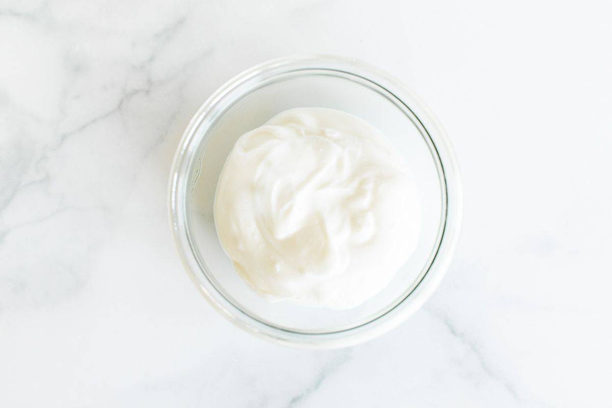 A small glass jar of creme fraiche replacement on a white marble surface.