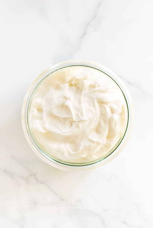 A small glass jar of creme fraiche substitute on a white marble surface.