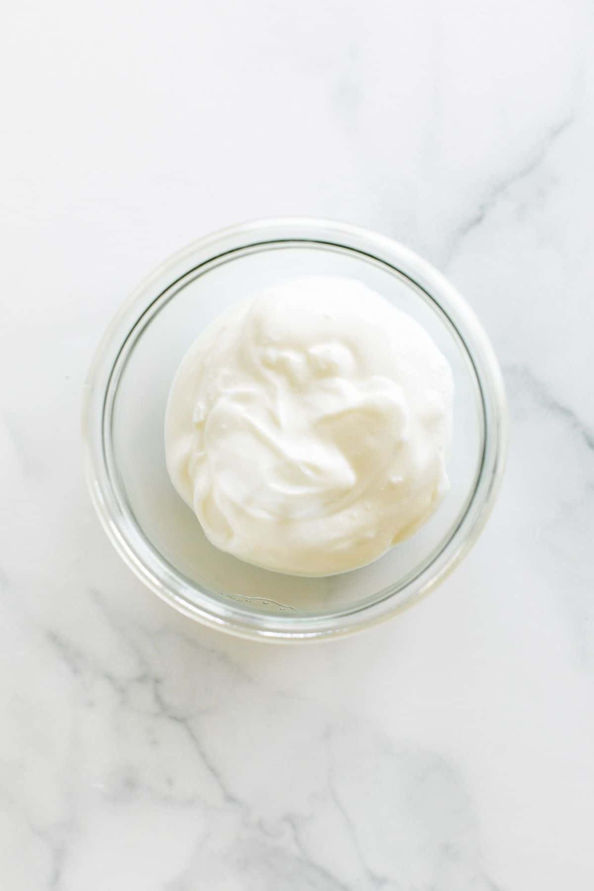 A small glass jar of creme fraiche alternative on a white marble surface.