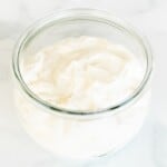 A small glass jar of creme fraiche substitute on a white marble surface.