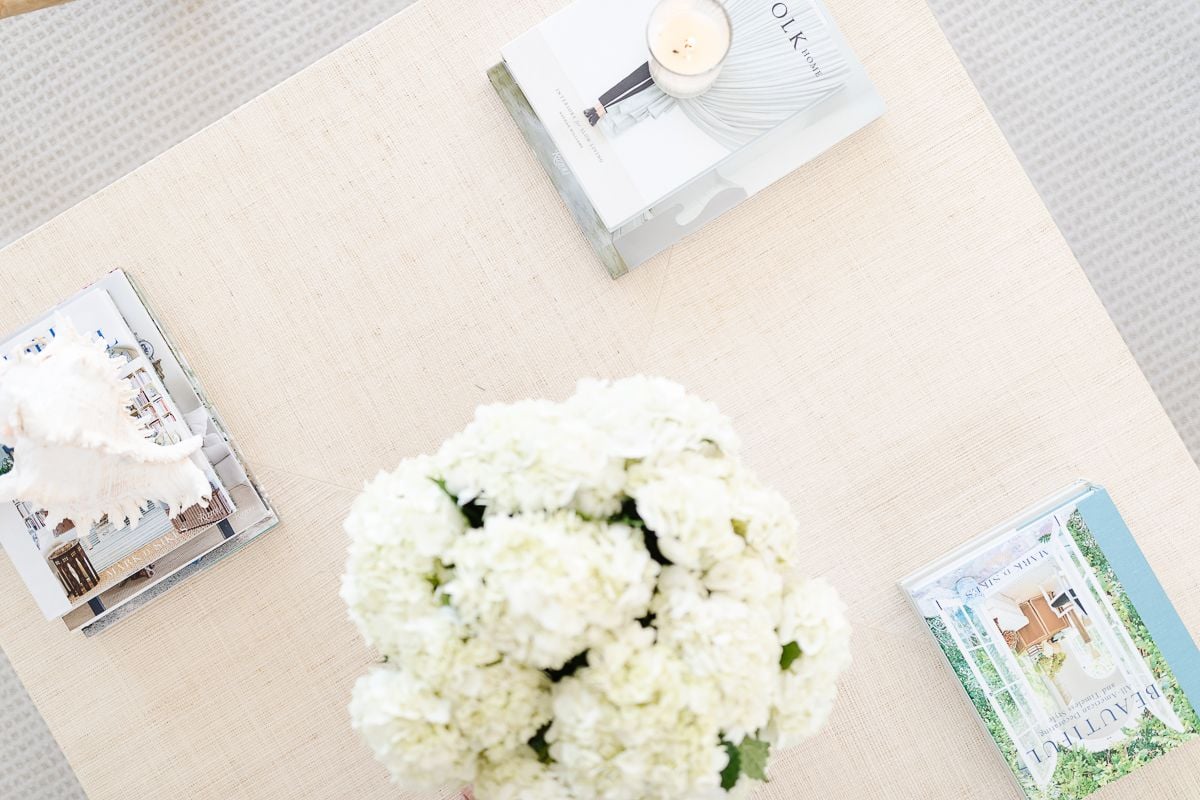 A raffia coffee table topped with white flowers and blue and white coffee table books