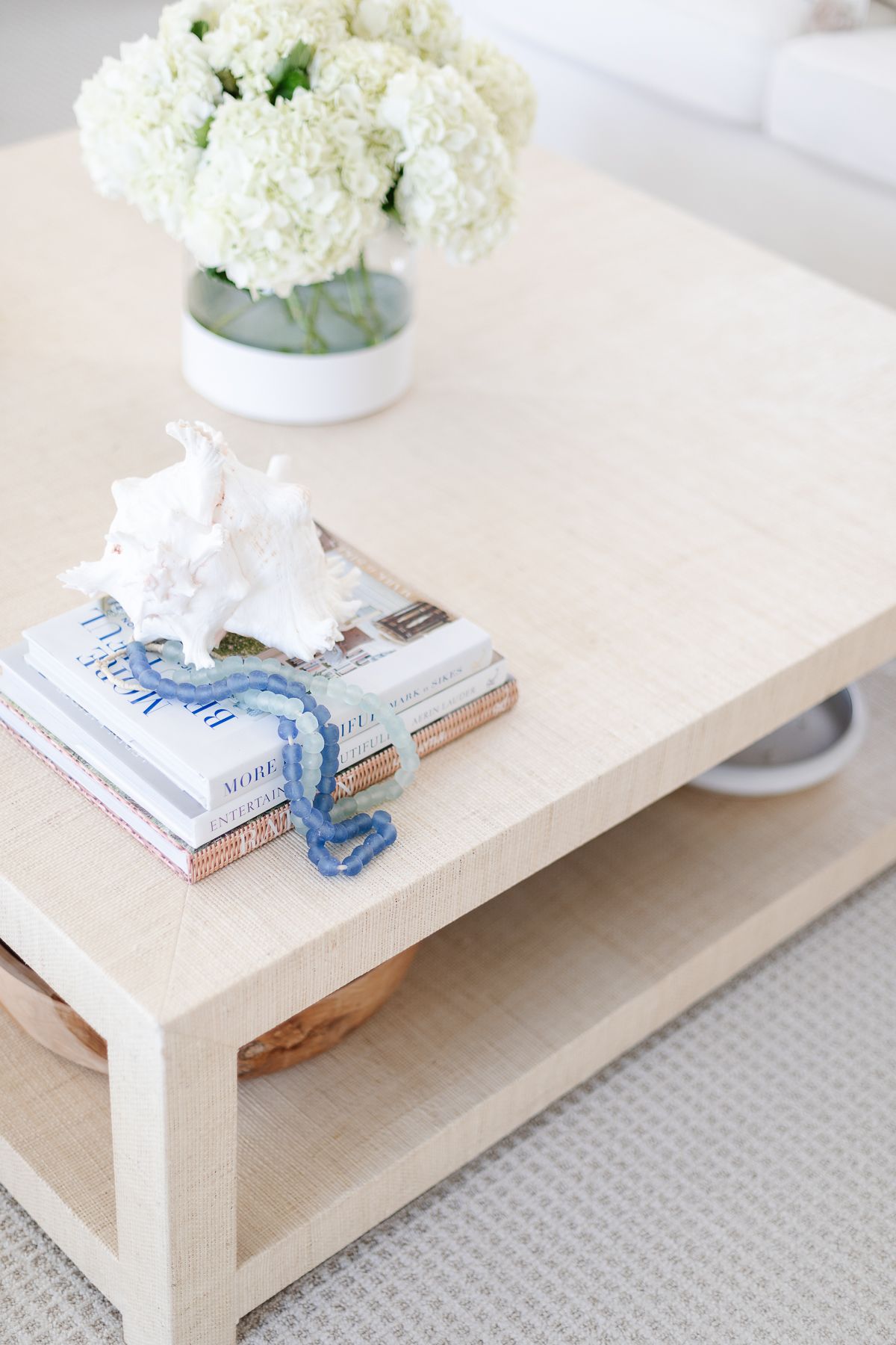 A raffia coffee table topped with white flowers and blue and white coffee table books