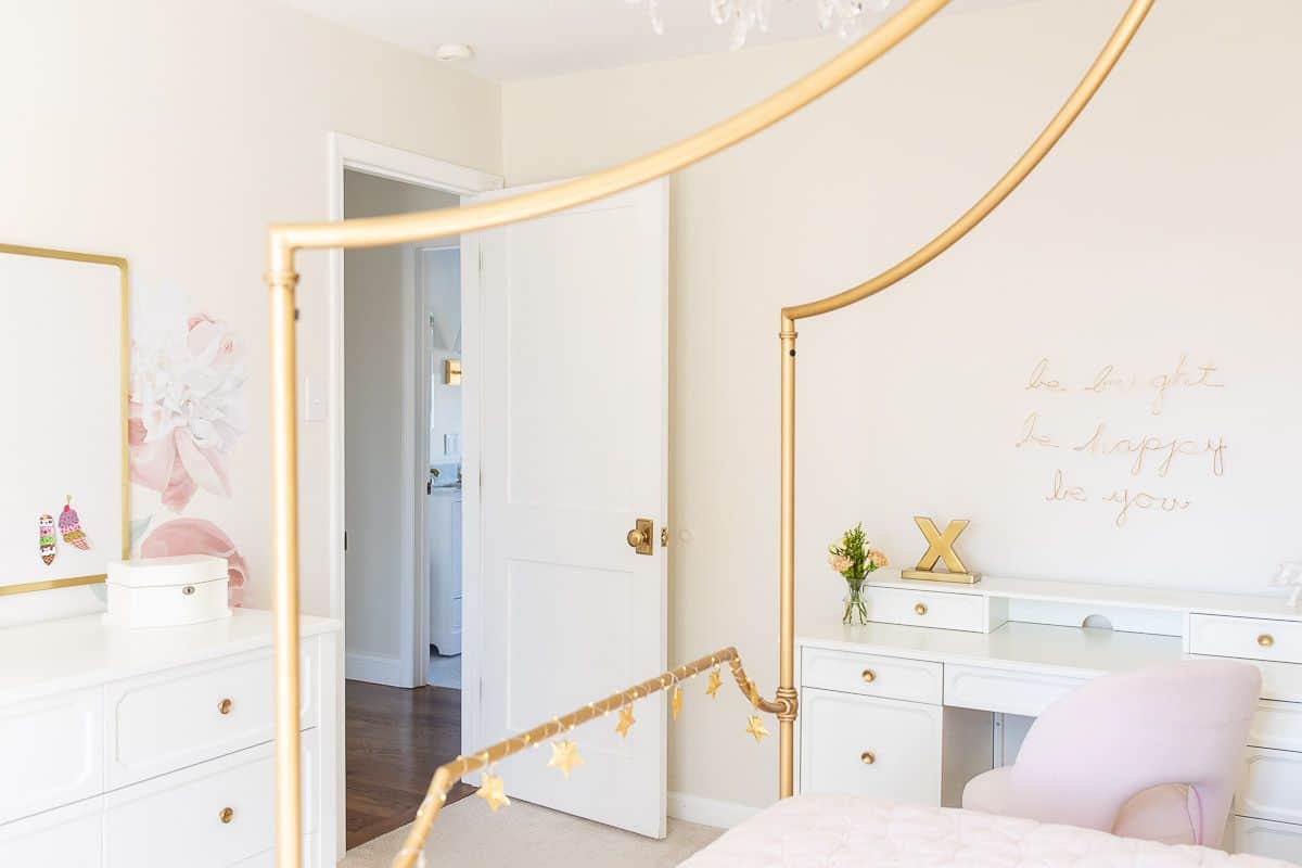 A teen girl's bedroom with a gold canopy bed and a white girls desk with pink chair