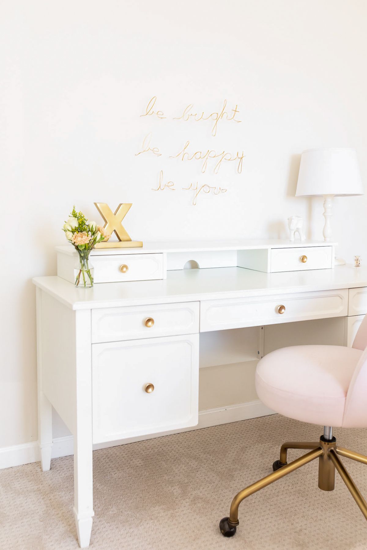 A white desk in a white bedroom, with a pink desk chair
