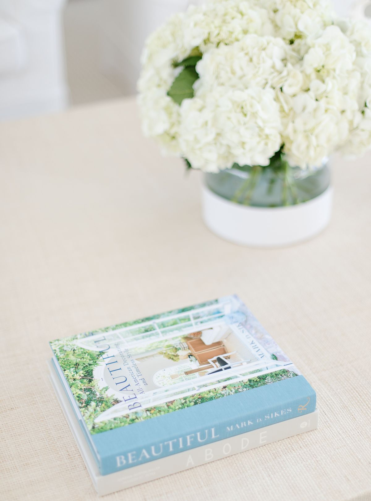 A raffia coffee table topped with white flowers and blue and white coffee table books