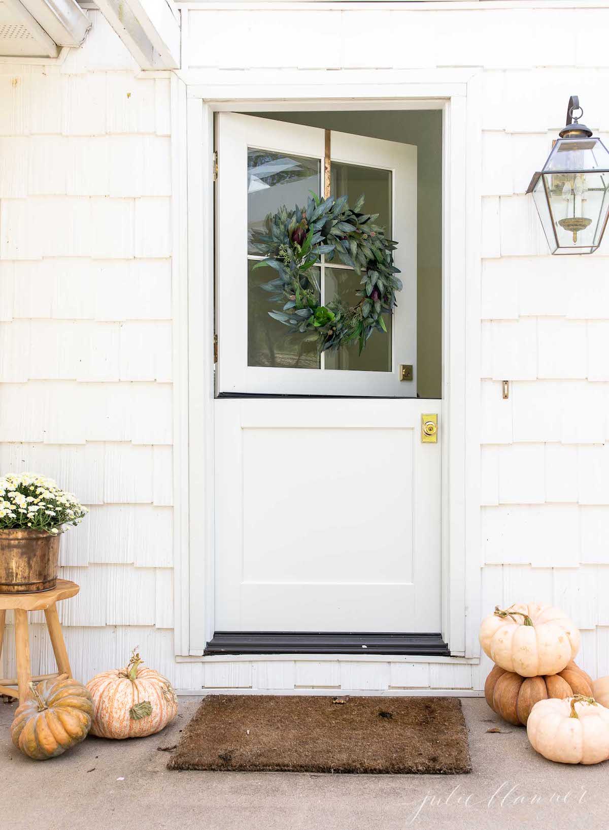 A minimalist fall decor featuring a white front door adorned with pumpkins and a wreath.