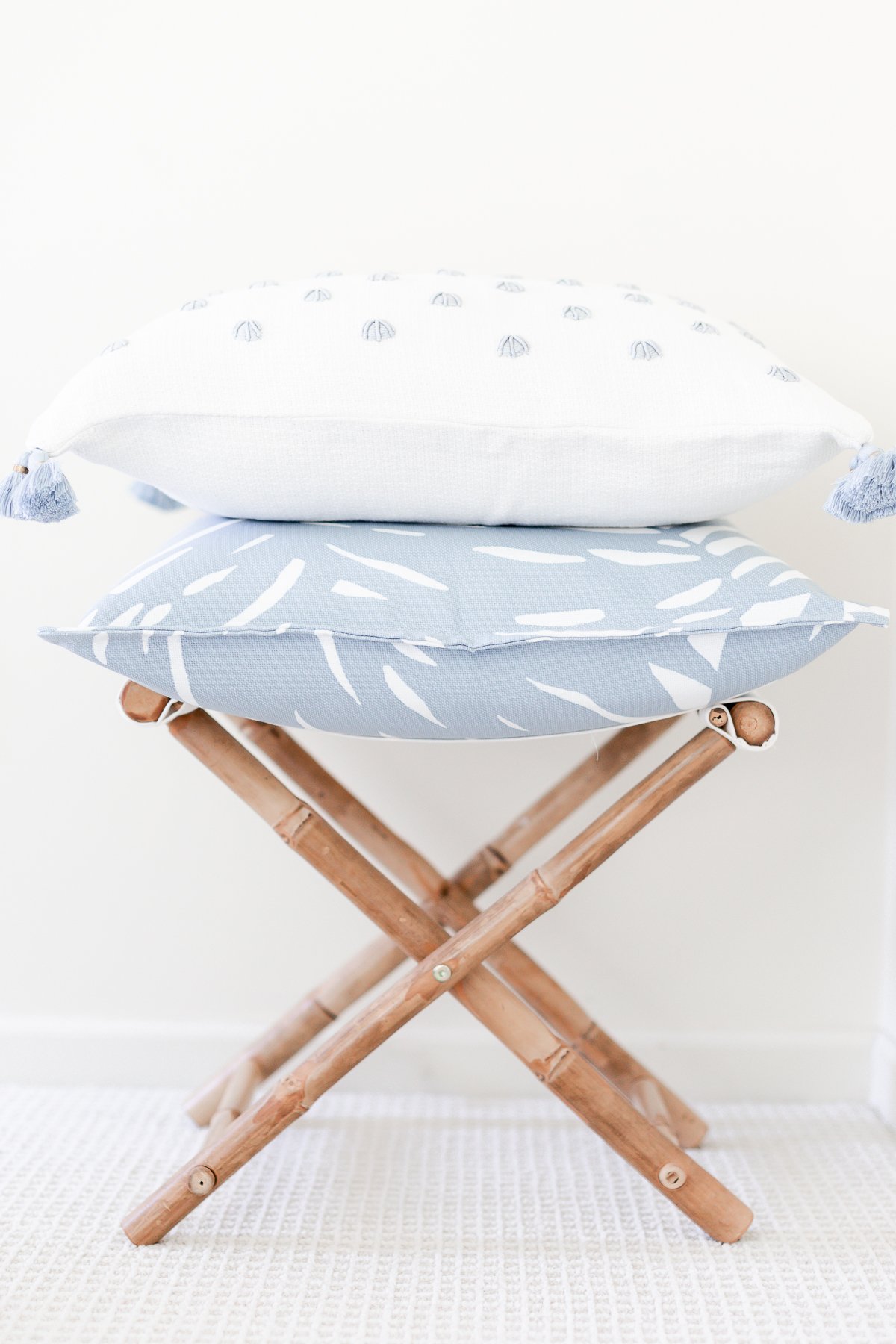 Two blue and white pillows with pillow inserts, stacked on a rattan stool.