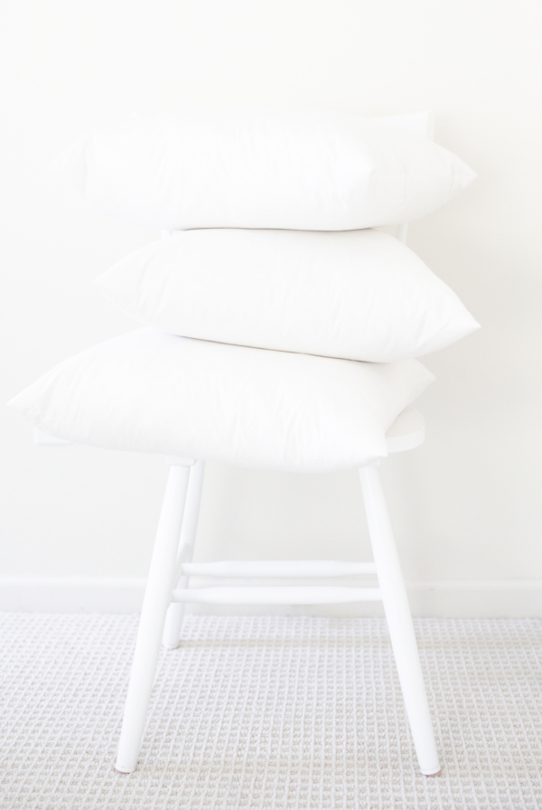 A stack of white pillow inserts on a white chair.